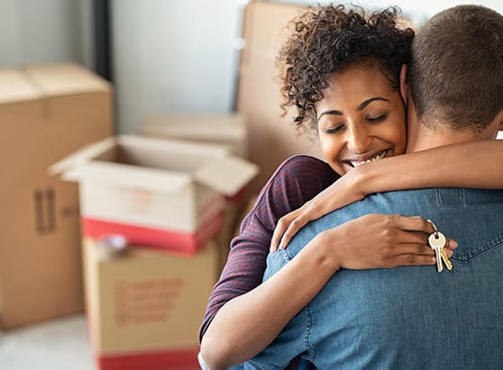 Couple who have just bought a new home, hugging next to moving boxes