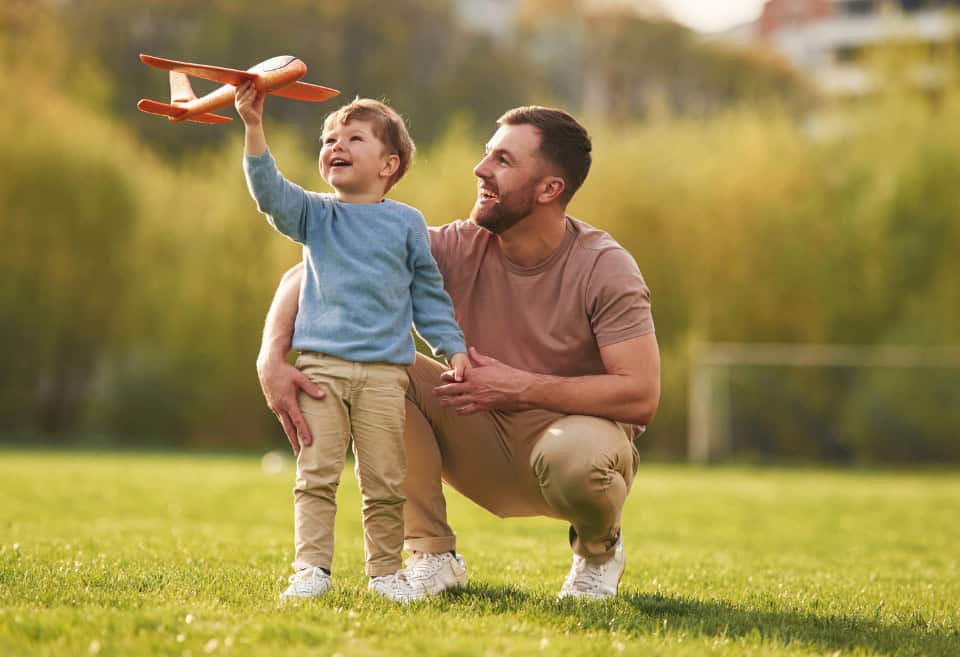 Father and son playing in park with toy airplane
